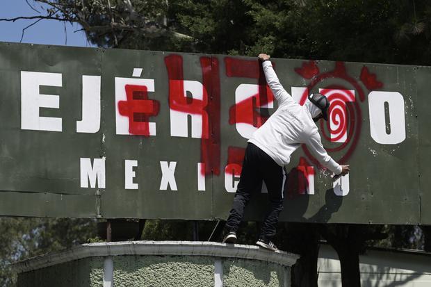 Un estudiante de Ayotzinapa pinta consignas en la entrada del Campamento Militar 1 durante una manifestación para exigir la extradición de un funcionario mexicano investigado por la desaparición de 43 estudiantes. (Foto de ALFREDO ESTRELLA /AFP).