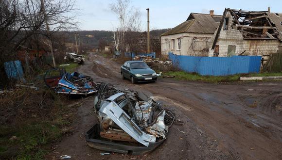Un automóvil recorre una calle con edificios residenciales gravemente dañados y automóviles destruidos en la aldea de Kamyanka de la región de Kharkiv el 25 de noviembre de 2022 en medio de la invasión rusa de Ucrania. (Foto de Anatolii Stepanov / AFP)
