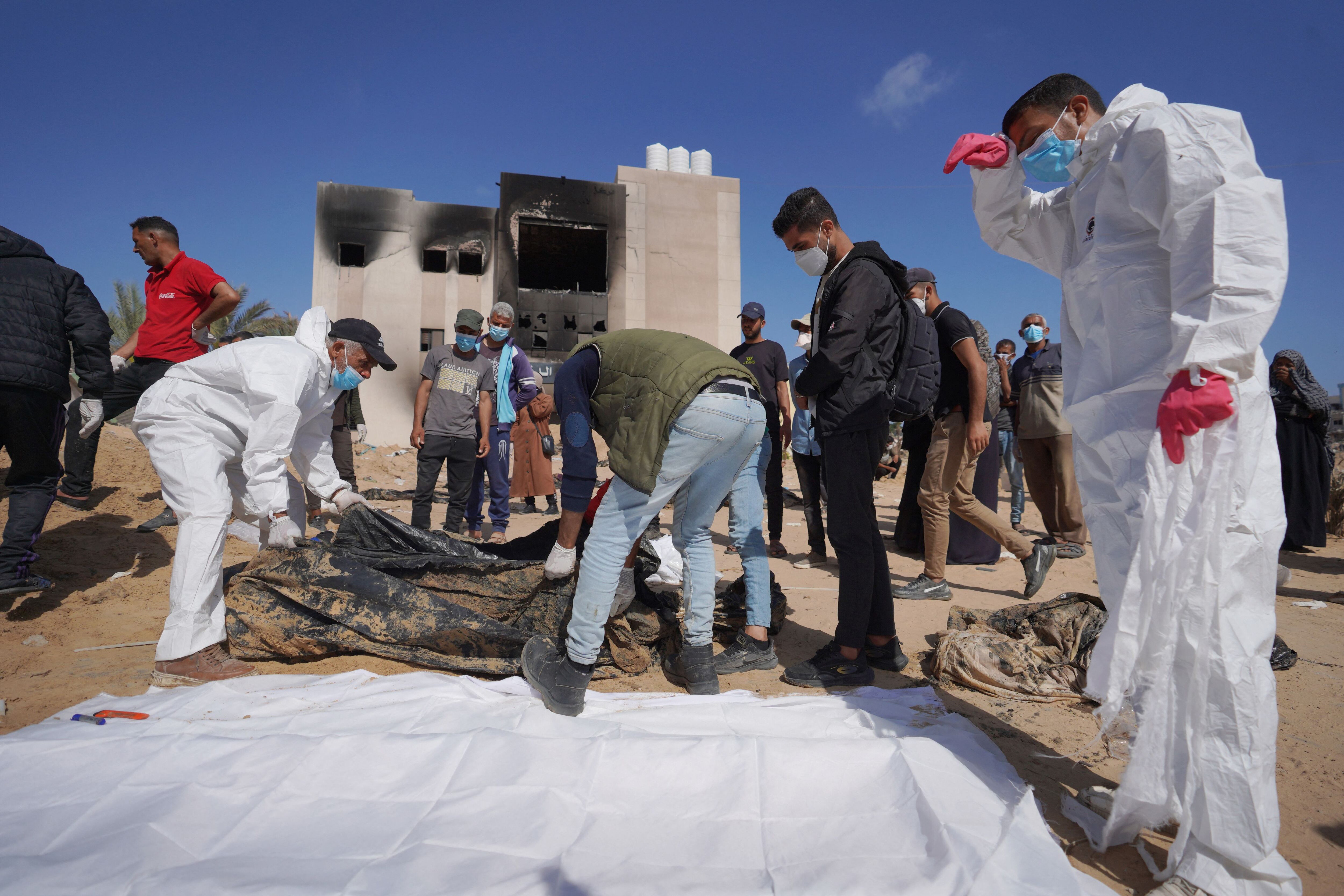 Trabajadores de la salud palestinos se encuentran junto a cuerpos que fueron enterrados por las fuerzas de Israel en el complejo hospitalario Nasser en Khan Yunis, en el sur de la Franja de Gaza. (Foto de AFP).