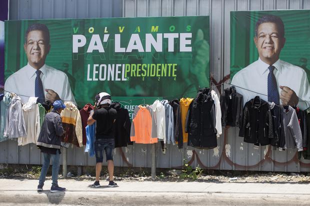 Two people look at pieces of clothing next to an electoral campaign poster of candidate Leonel Fernández in Santo Domingo.  (EFE/Orlando Barria).