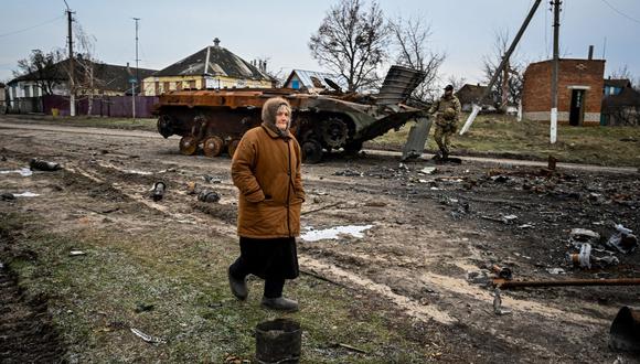 Una mujer pasa junto a un vehículo blindado destruido en la aldea liberada de Petropavlivka, cerca de Kupiansk, región de Kharkiv, Ucrania, el 15 de diciembre de 2022. (SERGEY BOBOK / AFP).