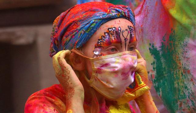 Una turista extranjera usa una máscara en medio del temor a la propagación del coronavirus en el festival de colores Holi. (AFP).