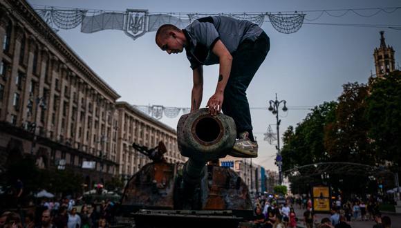 En esta fotografía tomada el 21 de agosto de 2022, un hombre se sube a un tanque ruso destruido en la calle Khreshchatyk en Kyiv, Ucrania, que se ha convertido en un museo militar al aire libre. (Dimitar DILKOFF / AFP).