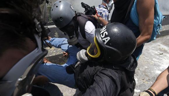 Un periodista que cubría las marchas de la oposición es asistido por un grupo de manifestantes, luego de que fuera agredido por la Guardia Bolivariana. (Foto: AFP)