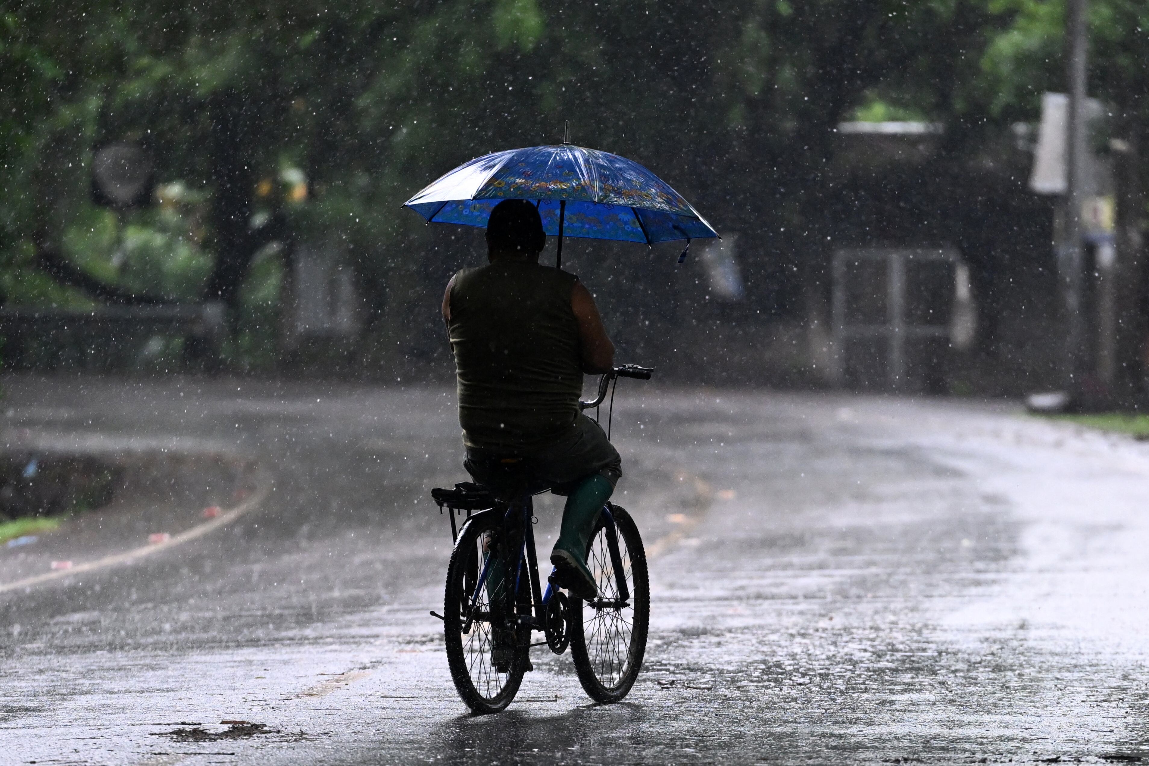 Un hombre anda en bicicleta bajo la lluvia durante la alerta roja decretada por el gobierno de El Salvador. (Foto de Marvin RECINOS / AFP).