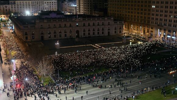 Gente levanta velas encendidas y teléfonos móviles frente al Palacio Presidencial de La Moneda mientras las mujeres marchan alrededor del edificio en Santiago el 10 de septiembre de 2023. (Foto de Pablo VERA / AFP)