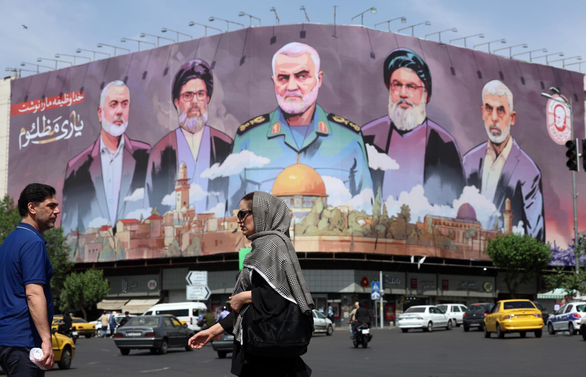 Iraníes pasan junto a una valla publicitaria con las fotos del difunto comandante de la Fuerza Quds Qasem Soleimani (C), los difuntos líderes de Hamás Ismail Haniyeh y Yahya Sinwar, entre otros. (EFE/EPA/ABEDIN TAHERKENAREH).