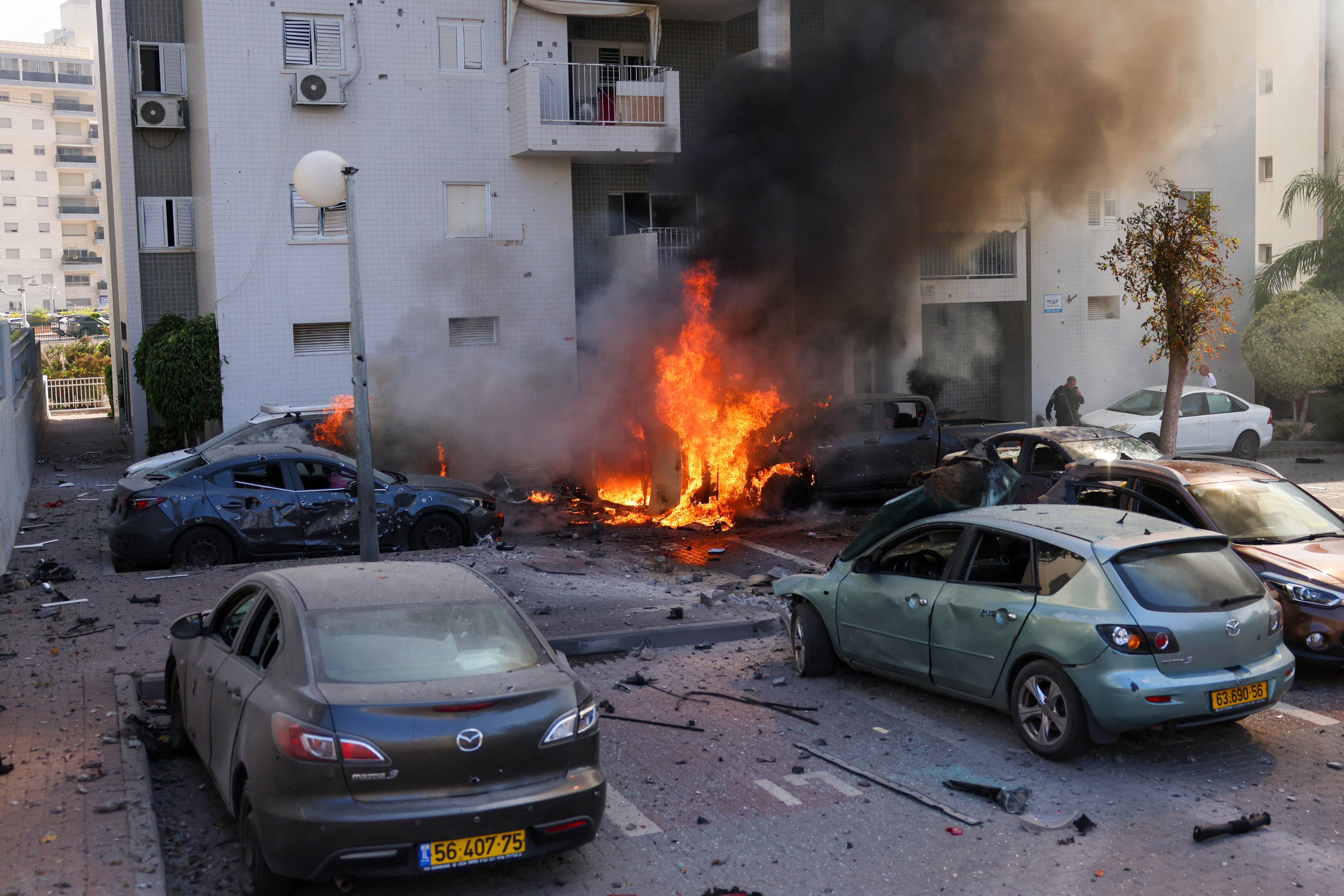 Un miembro de las fuerzas de seguridad israelíes se encuentra cerca de coches en llamas tras un ataque con cohetes desde la Franja de Gaza en Ashkelon, sur de Israel, el 7 de octubre de 2023.(Foto de Ahmad GHARABLI / AFP).