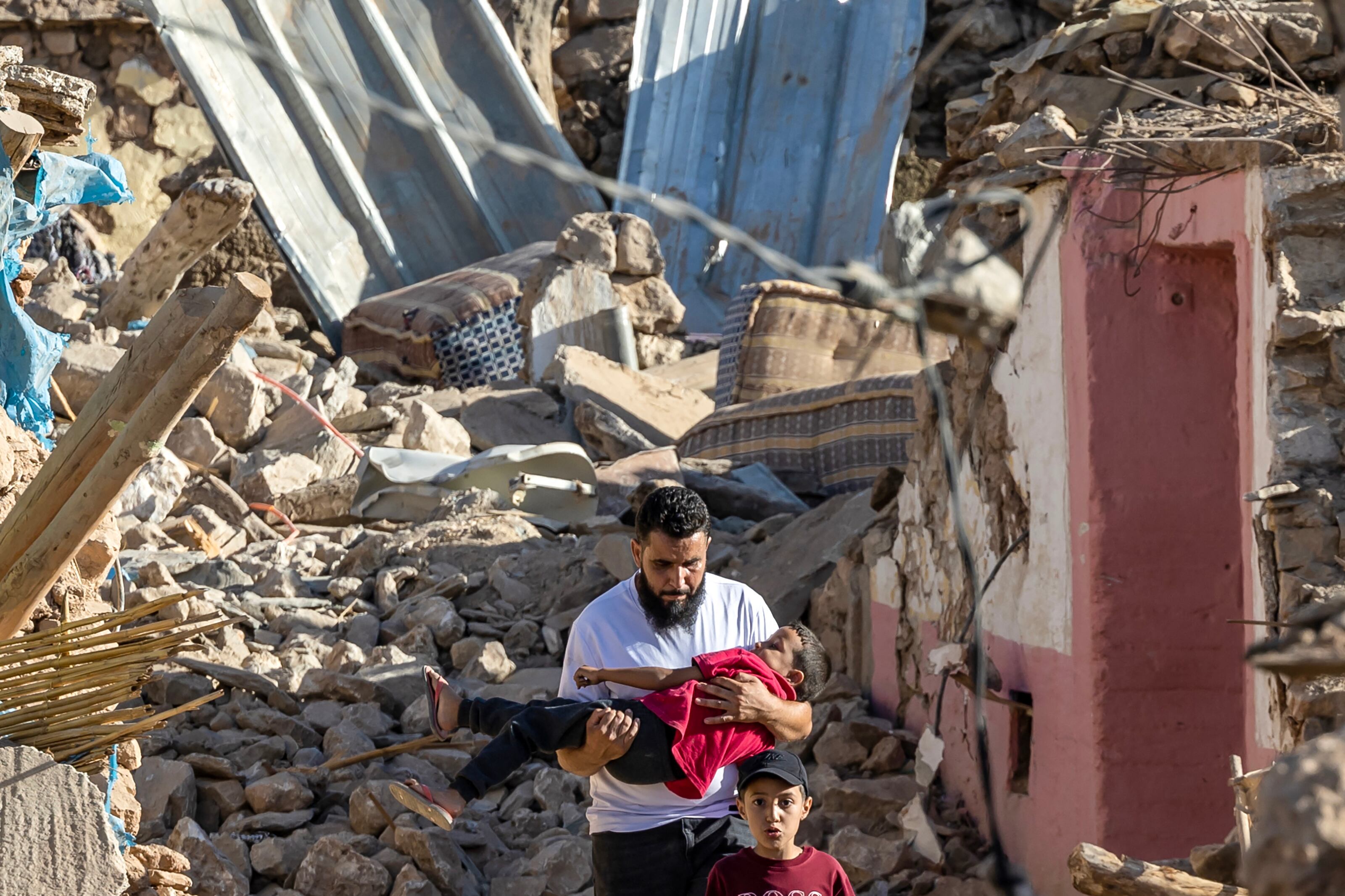 Un hombre lleva a un niño mientras pasa junto a casas destruidas después de un terremoto en el pueblo de montaña de Tafeghaghte, al suroeste de Marrakech, Marruecos, el 9 de septiembre de 2023. (Foto de Fadel SENNA / AFP).