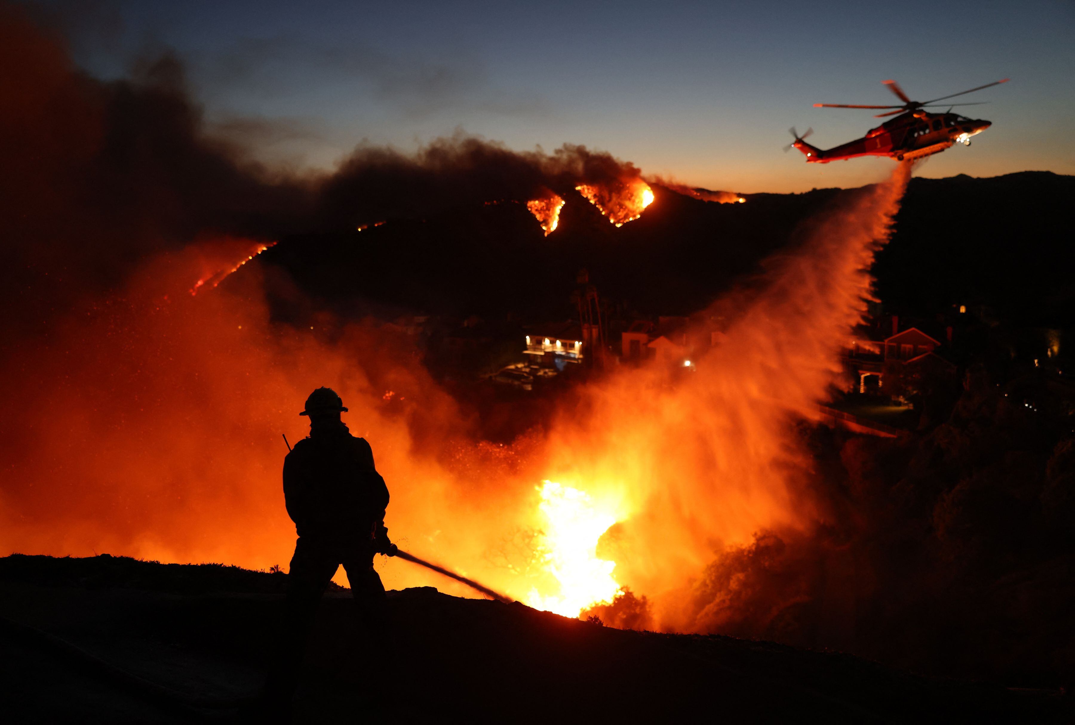 El personal de bomberos responde a las casas destruidas mientras un helicóptero lanza agua a medida que el incendio Palisades crece en Pacific Palisades, California, el 7 de enero de 2025. (Foto: David Swanson / AFP)