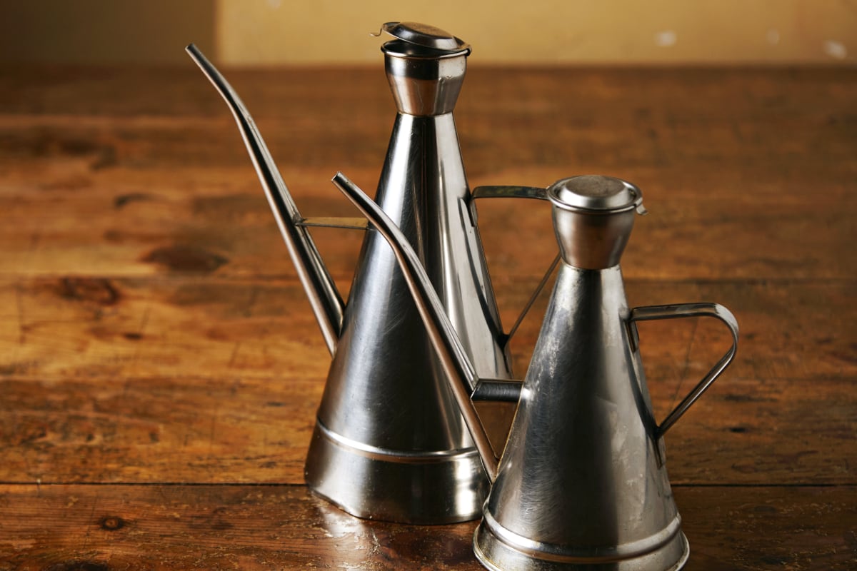 Dos dispensadores de aceite metal brillante de diferentes tamaños con boquillas largas. (Imagen: istock)