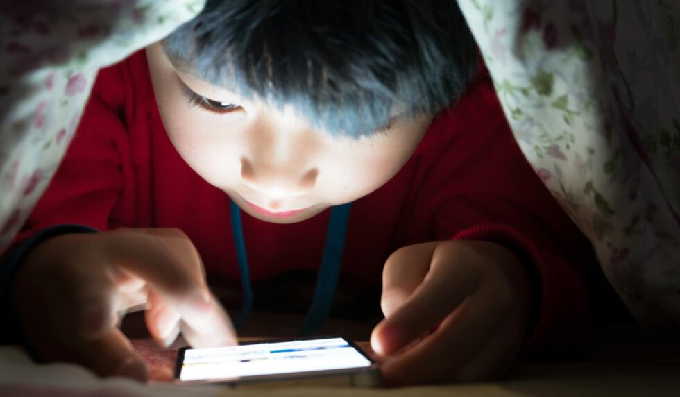 Niño en el teléfono celular bajo el edredón. (Imagen: istock)