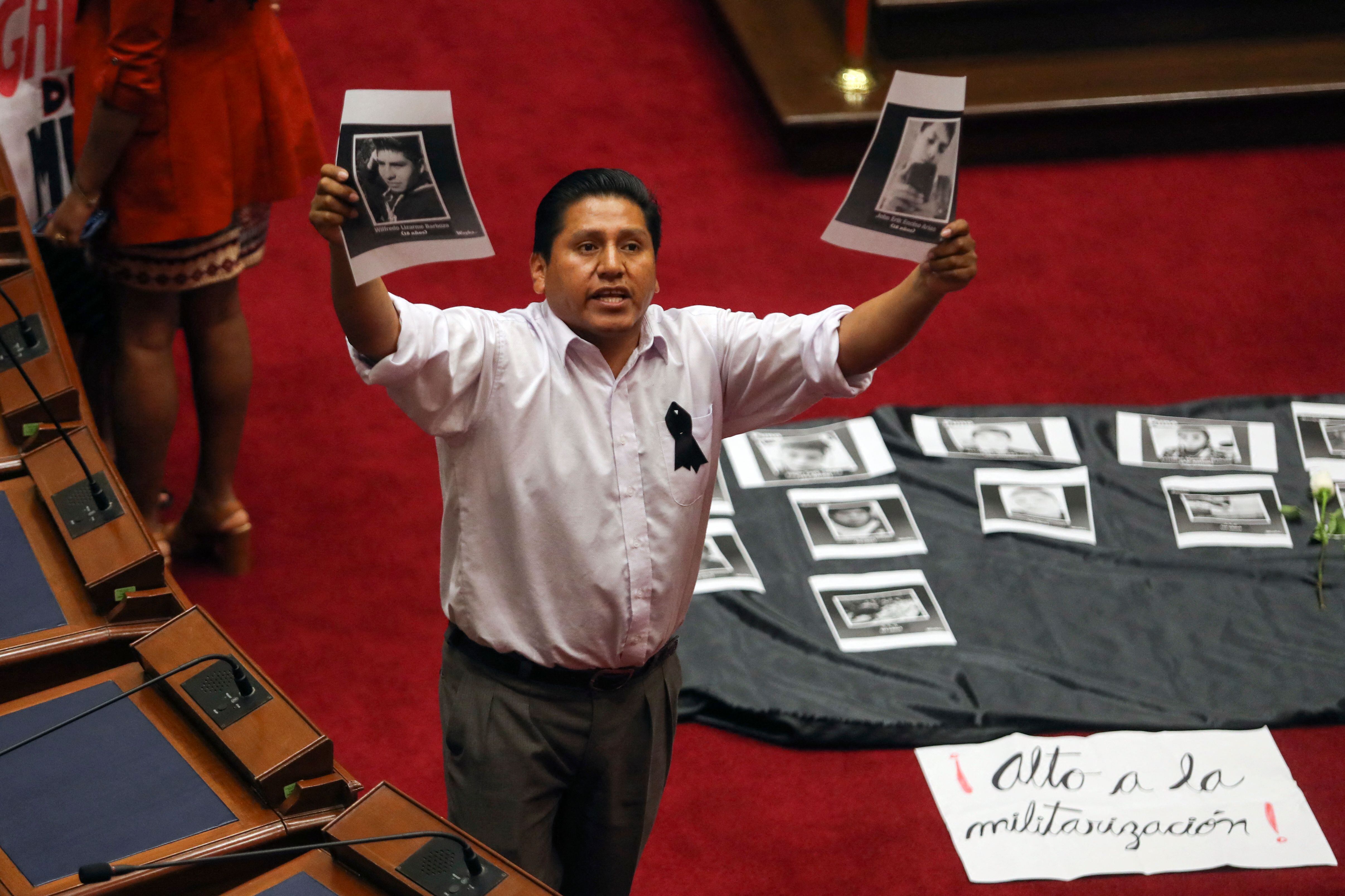 Peruvian congressman Wilson Quispe of the leftist Peru Libre party holds pictures of people killed during recent anti-government protests as chief of staff Alberto Otarola speaks at the plenary session of the Congress in Lima on January 10, 2023. Protests against Peru's president, Dina Boluarte, which have left 40 people dead in a month, continue on Tuesday with road blockades in six regions of the country as the new cabinet goes to Congress to ask for a vote of confidence in its inauguration. (Photo by SEBASTIAN CASTANEDA / POOL / AFP)