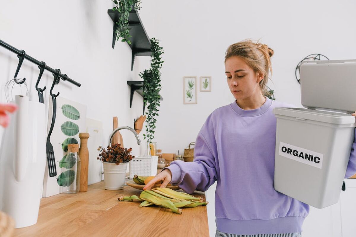Una mujer metiendo las cáscaras de plátano a un bote de basura. | Imagen referencial: SHVETS production / Pexels
