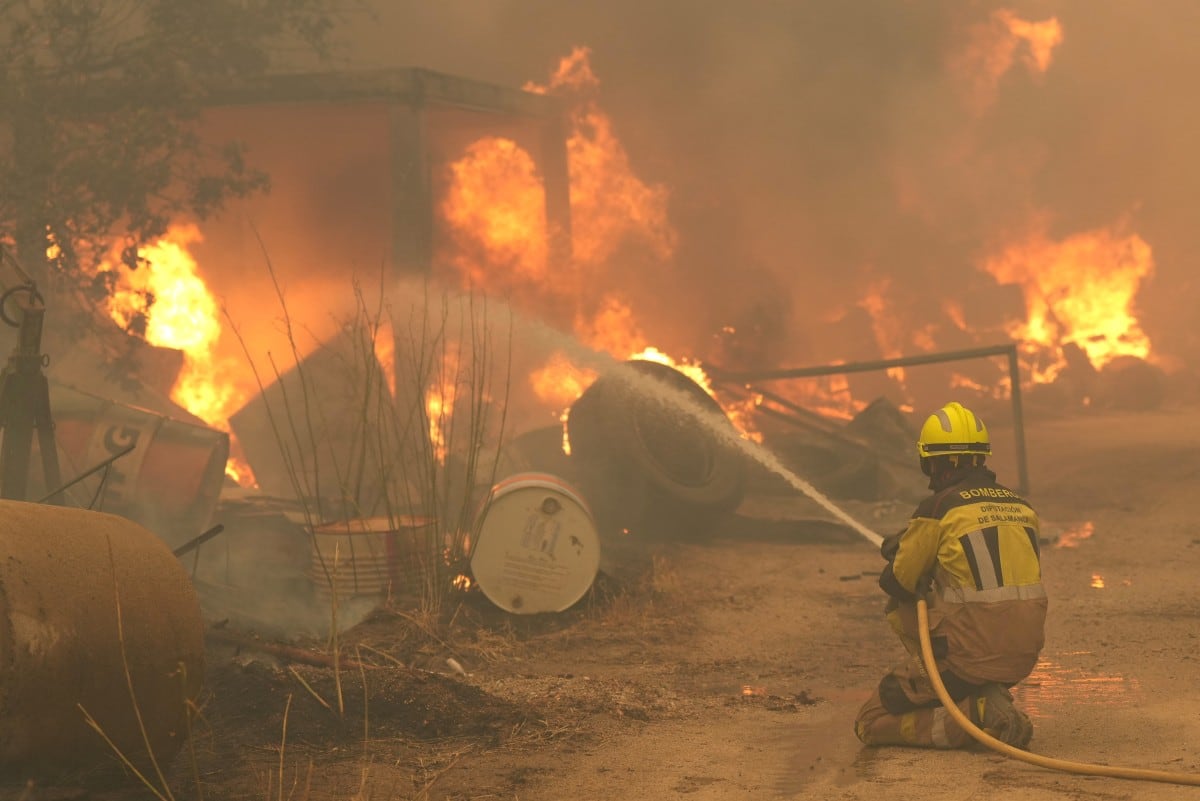 Un bombero riega neumáticos y barriles en llamas mientras combate un incendio forestal en la zona de Cebreros, cerca de Ávila, a 80 km al oeste de Madrid, el 24 de julio de 2026. (Cesar MANSO / AFP)