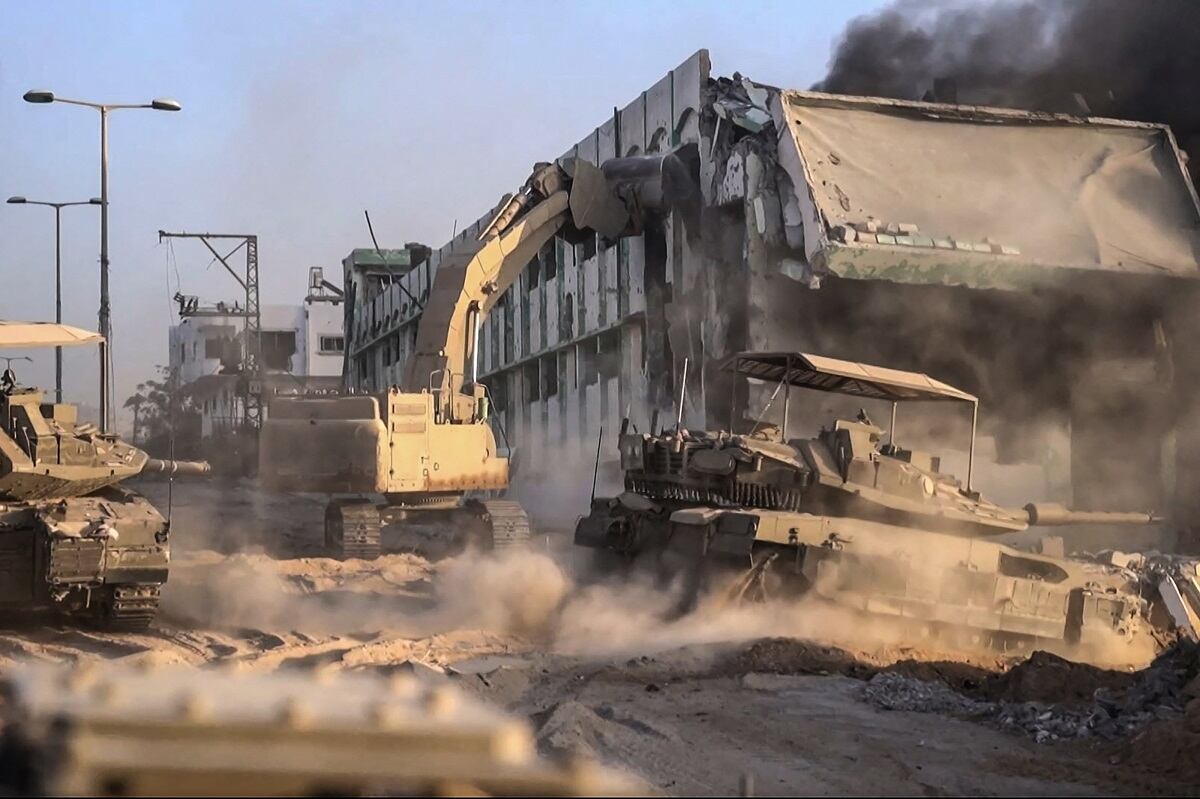 Tanques israelíes rodando mientras una topadora del ejército derriba un edificio en llamas dentro de la Franja de Gaza, el 11 de noviembre de 2023. (Foto de Armada israelí / AFP)