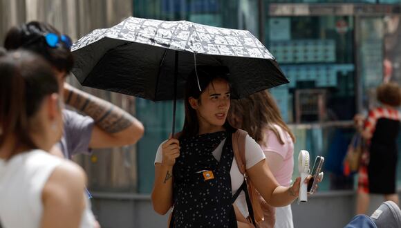 Una mujer con un bebé se protege del sol con un paraguas mientras sostiene un ventilador para combatir el calor en medio de una ola de calor en Madrid el 9 de agosto de 2023. (Foto de JAVIER SORIANO / AFP)