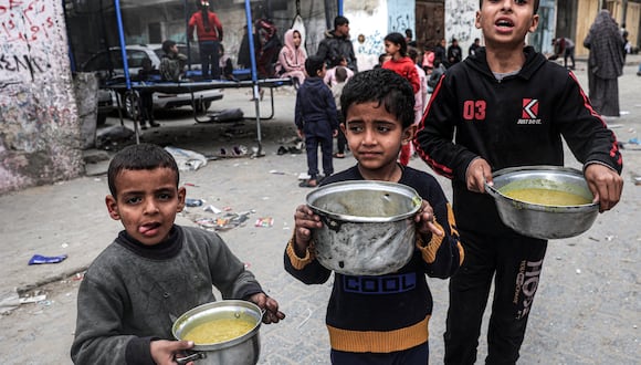 Los niños sostienen ollas llenas de comida proporcionada por una organización benéfica en Rafah, en el sur de la Franja de Gaza, el 16 de marzo de 2024. (Foto de SAID KHATIB / AFP).