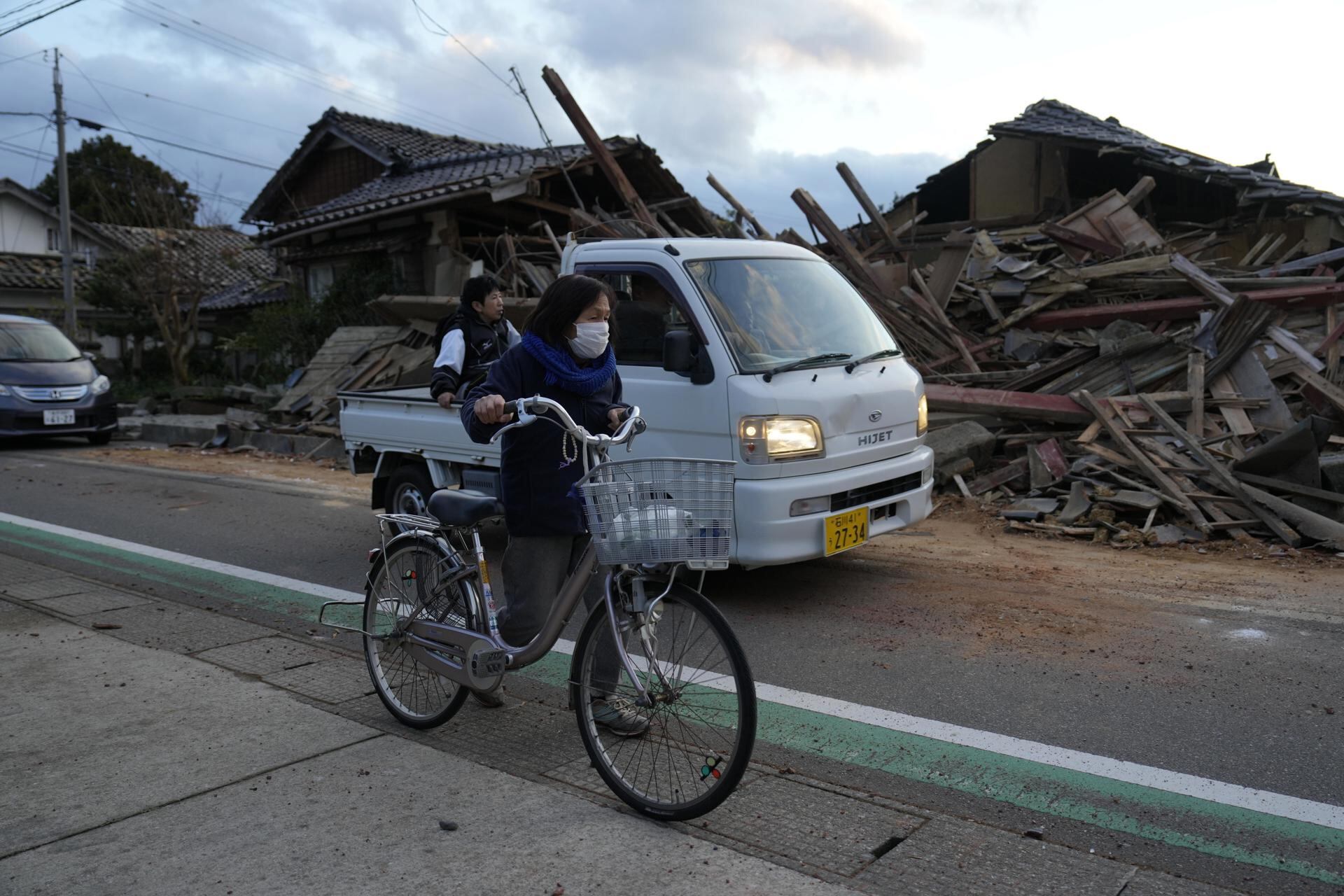 Una mujer empuja su bicicleta junto a un edificio derrumbado después de un fuerte terremoto en la ciudad de Togi, Península de Noto, Japón, el 2 de enero de 2024. (EFE/EPA/FRANCK ROBICHON).