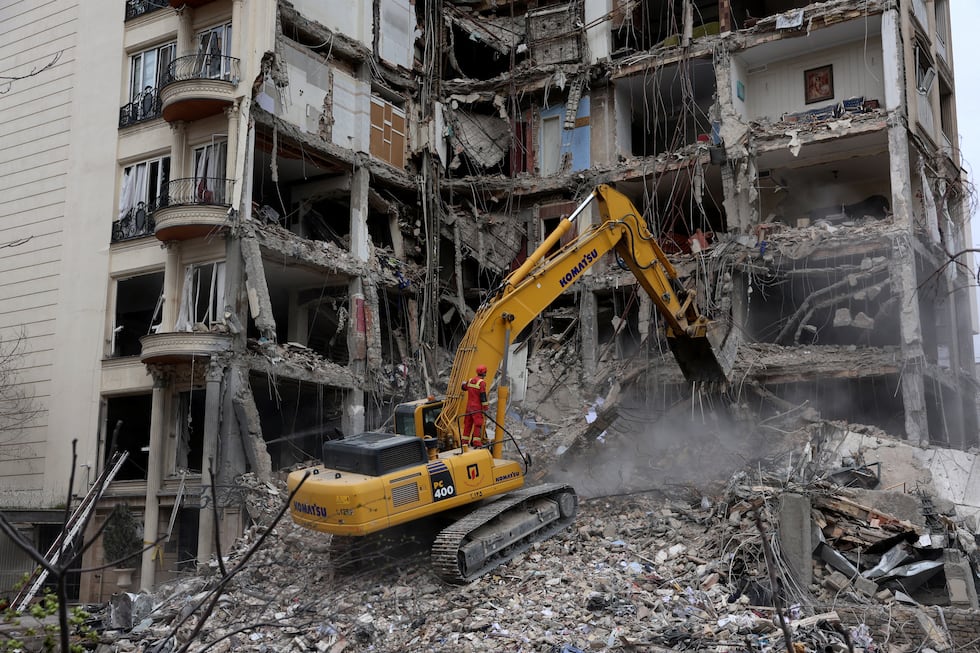 Bomberos de Irán, con la ayuda de una excavadora, retiran escombros de un edificio residencial destruido en el norte de Teherán el 23 de marzo de 2026. (Foto de AFP).