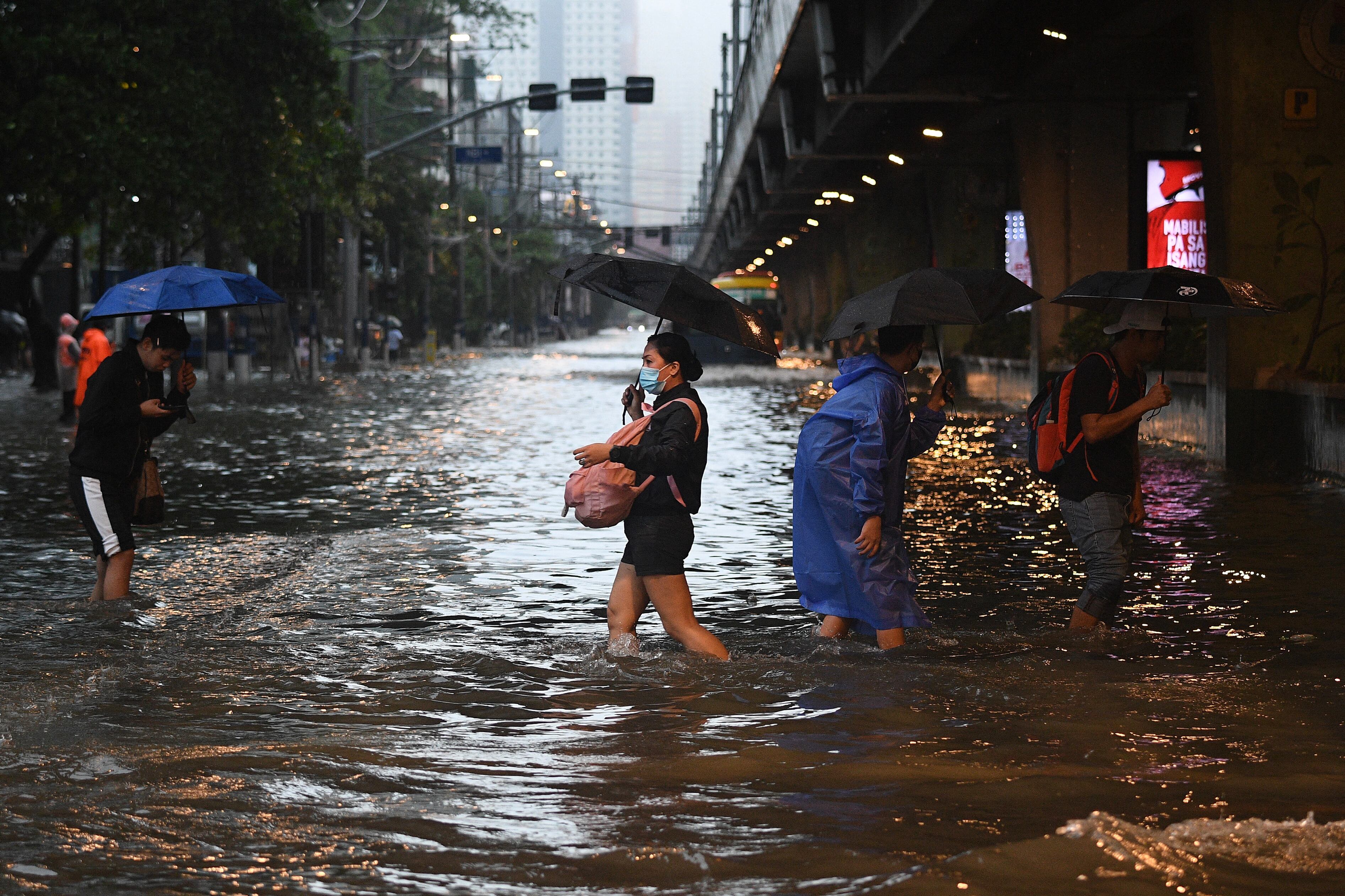 Los peatones cruzan una calle inundada en Manila el 24 de julio de 2024 en medio de las fuertes lluvias provocadas por el tifón Gaemi. Una lluvia incesante empapó el norte de Filipinas el 24 de julio. (Foto de Ted ALJIBE / AFP).