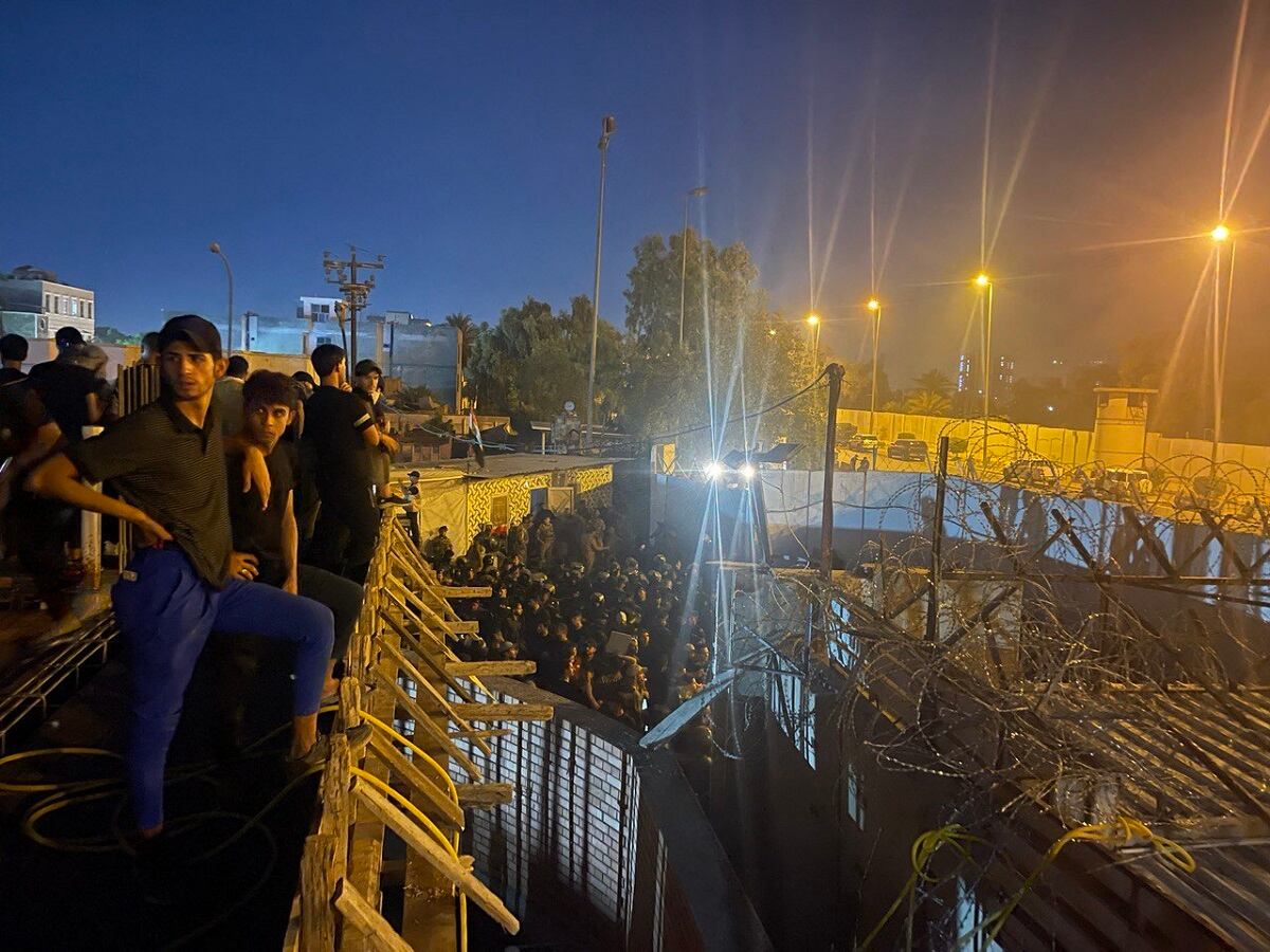 Manifestantes se paran en la parte superior de un edificio con vista a una calle llena de policías antidisturbios iraquíes que conducen a la embajada sueca en Bagdad el 20 de julio de 2023. (Foto de Ammar Karim / AFP)