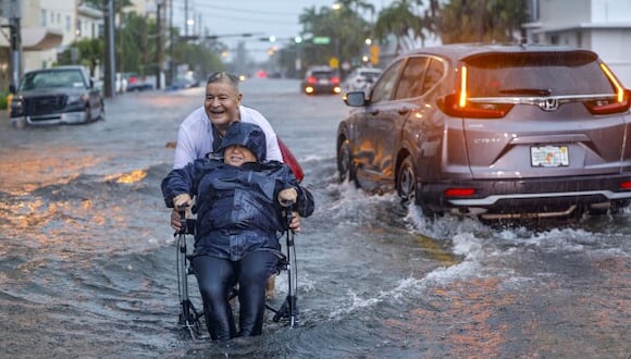 Víctor Corone empuja a su esposa en silla de ruedas en una calle inundada de Miami Beach, Florida, el 12 de junio del 2024. (Al Diaz, Miami Herald vía AP).