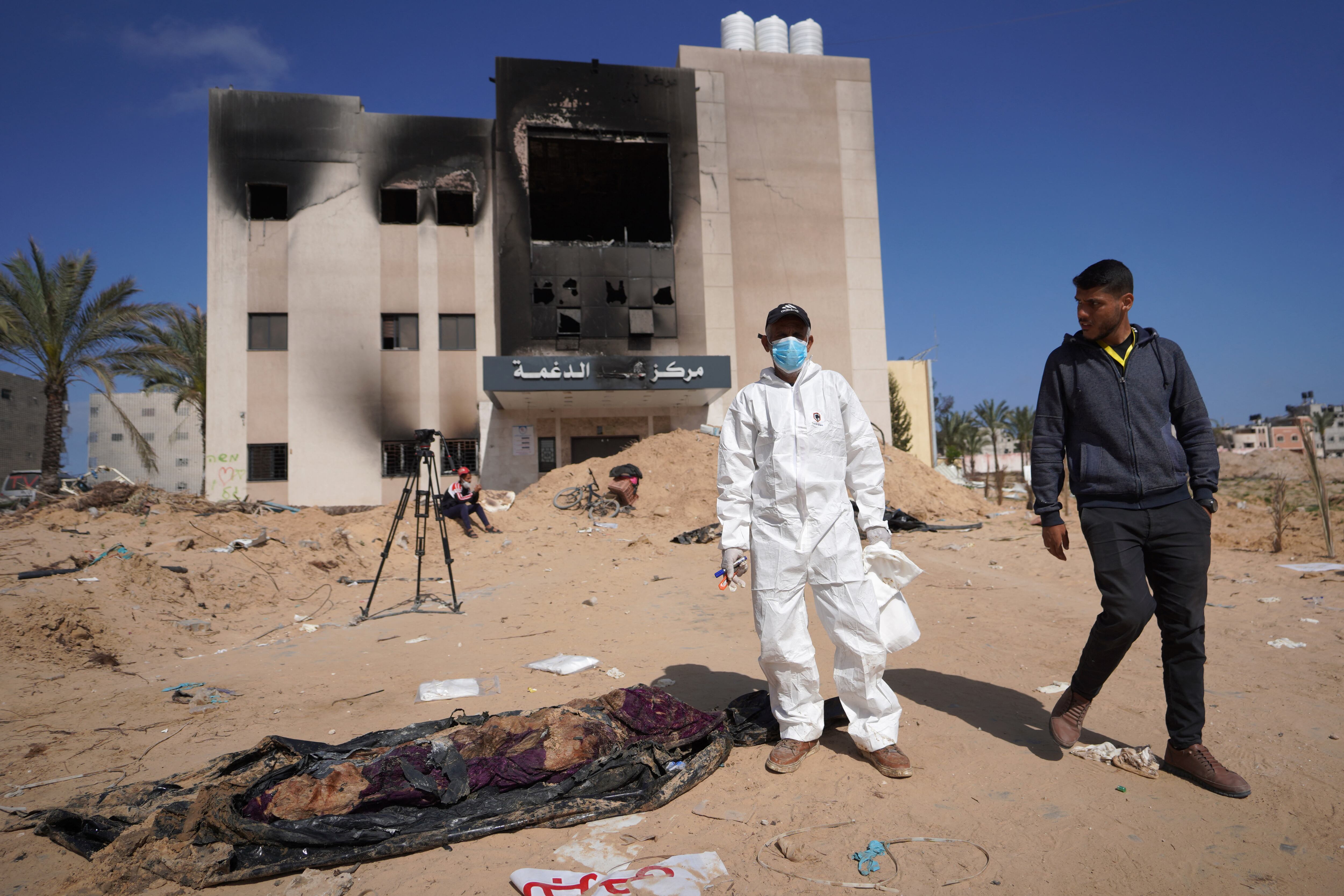 Trabajadores de la salud palestinos se encuentran junto a cuerpos que fueron enterrados por las fuerzas de Israel en el complejo hospitalario Nasser en Khan Yunis, en el sur de la Franja de Gaza. (Foto de AFP).
