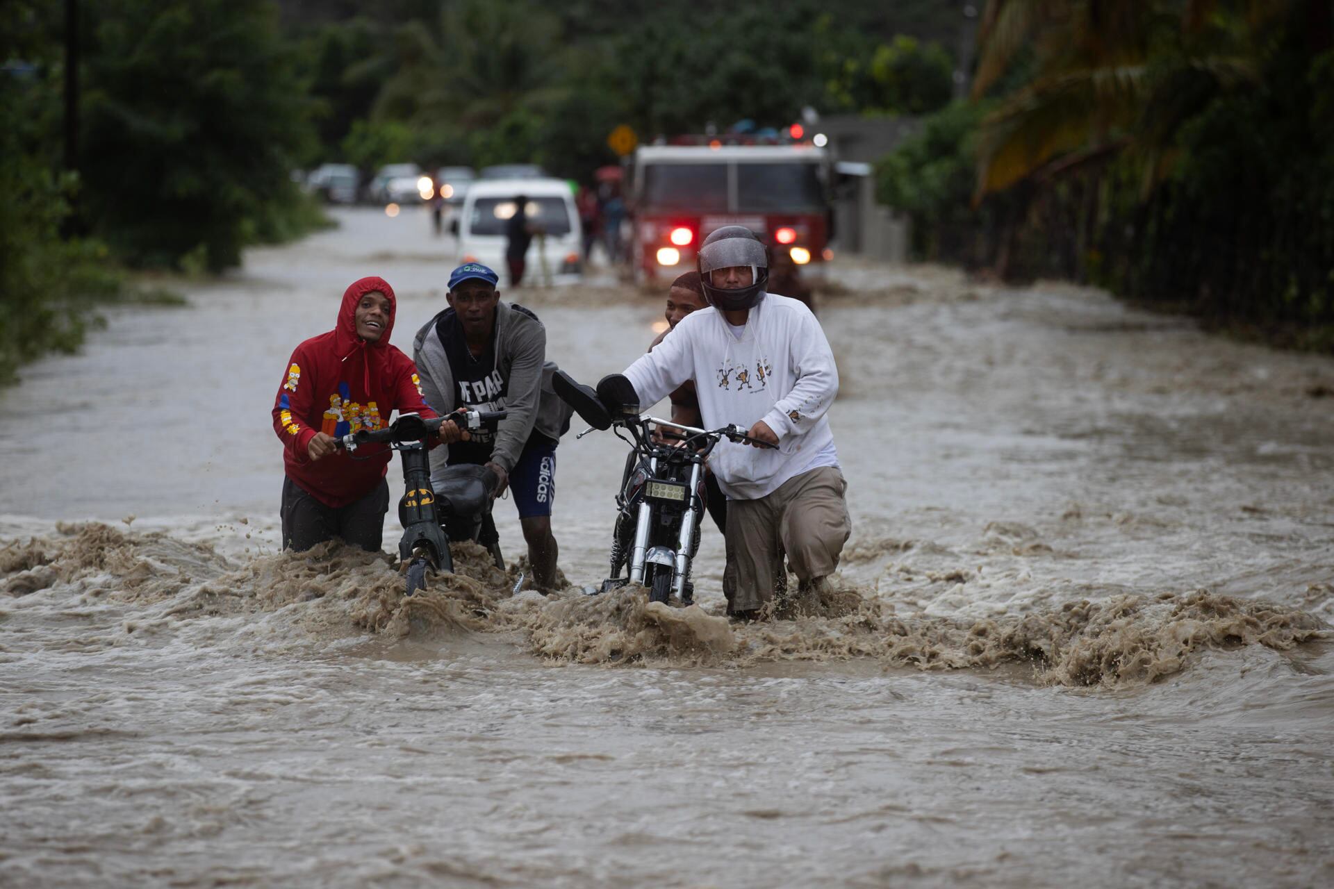 Personas cruzan con dificultad la carretera que se encuentra inundada producto de las intensas lluvias en San José de Ocoa, República Dominicana.  (EFE/Orlando Barría).