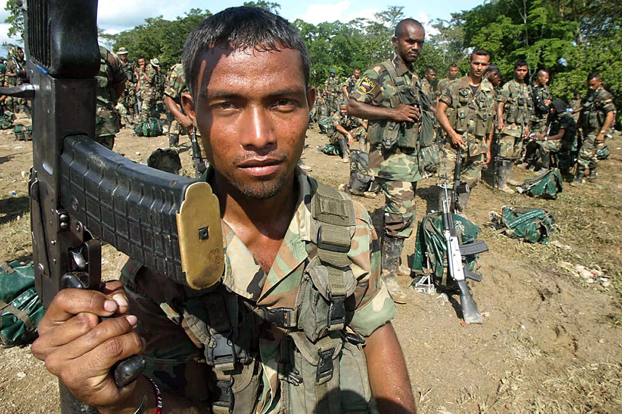 Un miembro de las derechistas Autodefensas Unidas de Colombia (AUC), levanta su arma durante una ceremonia en el campamento base Dos en Tibú, el 10 de diciembre de 2004. (Foto de LUIS ACOSTA/AFP).