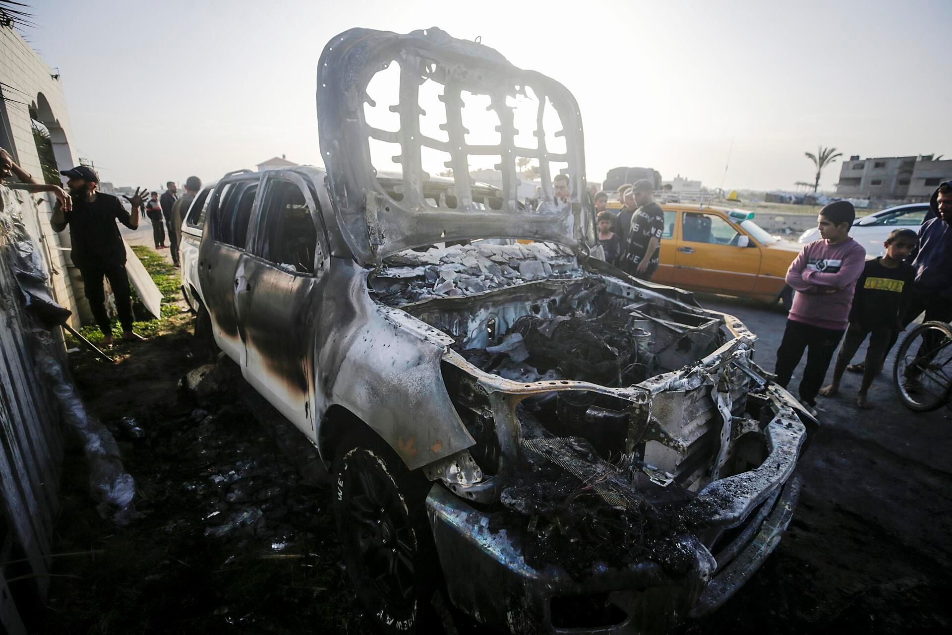 La gente observa el automóvil destruido de la ONG World Central Kitchen (WCK) a lo largo de la carretera Al Rashid, entre Deir Al Balah y Khan Younis, en el sur de la Franja de Gaza. (EFE/MOHAMMED SABER).