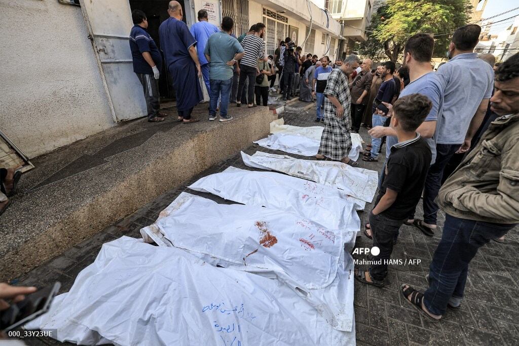 La gente espera junto a bolsas para cadáveres afuera de la morgue del hospital al-Shifa en la ciudad de Gaza el 12 de octubre de 2023. (Foto de Mahmud HAMS / AFP).