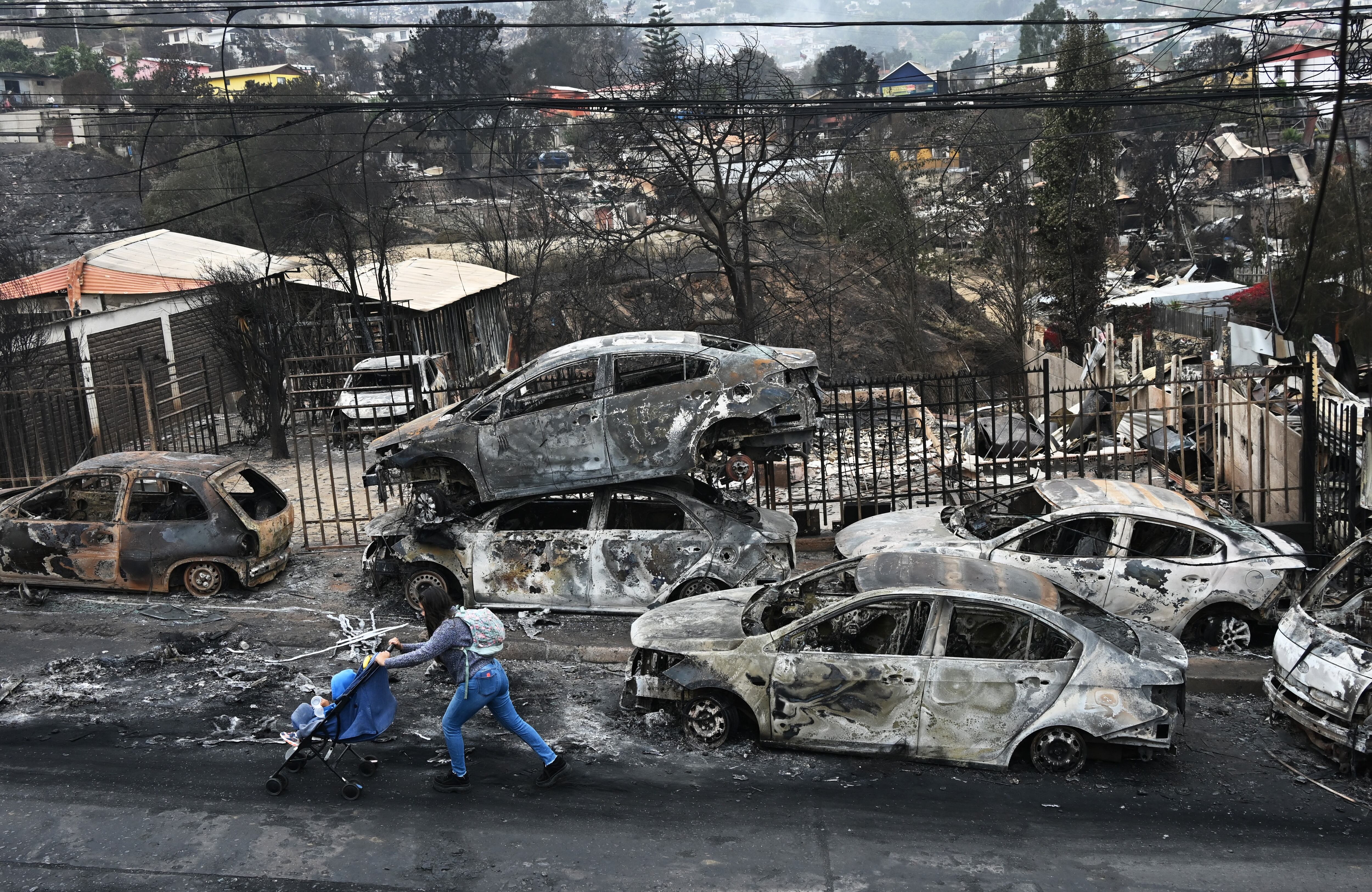 Una mujer con su bebé pasa junto a vehículos quemados después de un incendio forestal en Quilpue, región de Valparaíso, Chile, el 4 de febrero de 2024. (Foto de RODRIGO ARANGUA/AFP).