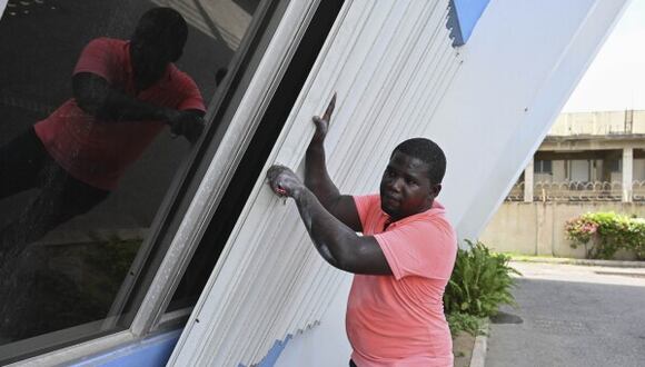 Un hombre cubre las ventanas de un edificio para protegerlas de la llegada del huracán Beryl, en Kingston, Jamaica, el 2 de julio de 2024. (AP Foto/Collin Reid)