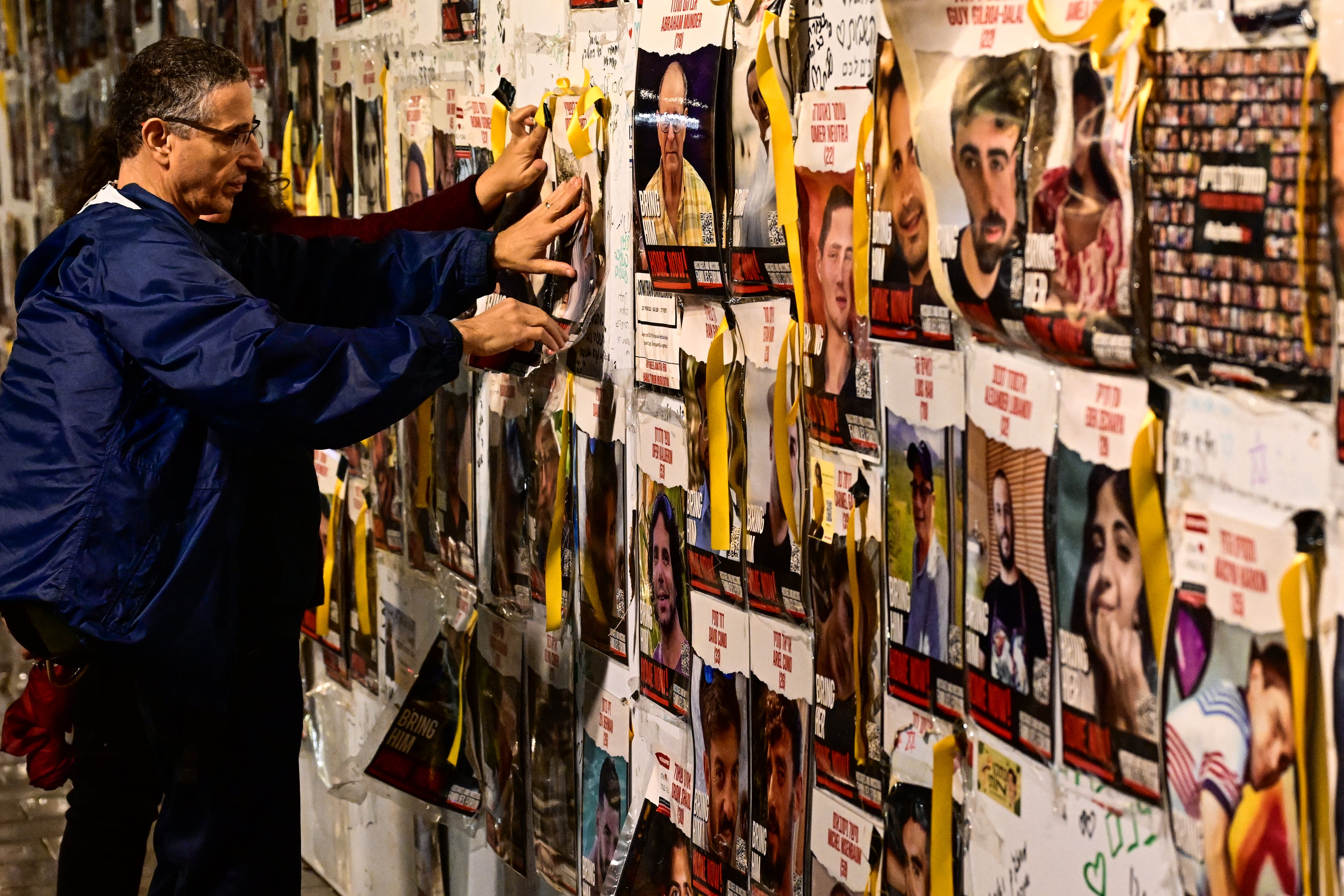 Un manifestante añade un retrato en la pared durante una manifestación de partidarios y familiares de rehenes israelíes retenidos en Gaza desde el ataque del 7 de octubre en Tel Aviv el 23 de diciembre de 2023, en medio de batallas en curso entre Israel y el grupo palestino Hamas. (Foto de Alberto PIZZOLI / AFP)
