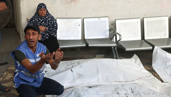 Un empleado palestino que trabaja como guardia para las Naciones Unidas reacciona mientras se agacha junto a los cuerpos cubiertos de sus familiares de la familia al-Hamayda después de que fueron llevados al hospital Al-Najjar tras un ataque aéreo israelí en Rafah, en el sur de la Franja de Gaza. (Foto de SAID KHATIB / AFP)