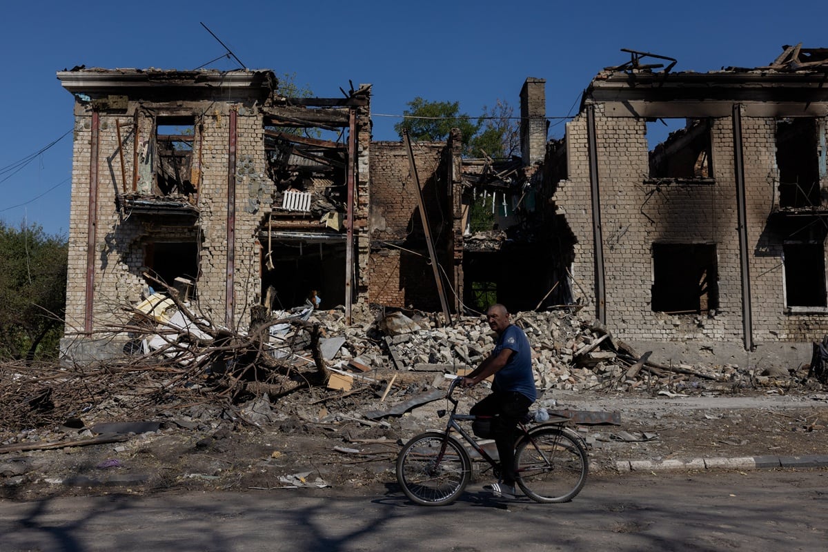 Un hombre pasa en bicicleta junto a un edificio residencial dañado en Novodonets'ke, región de Donetsk, el 14 de septiembre de 2025, en medio de la invasión rusa de Ucrania. (Foto de Tetiana DZHAFAROVA / AFP)