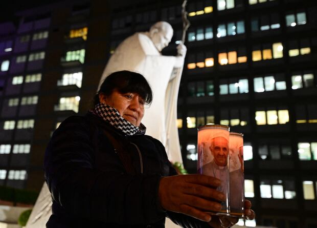 Una fiel de Bolivia sostiene velas con la foto del papa Francisco afuera del hospital Gemelli. (Foto de Tiziana FABI / AFP).