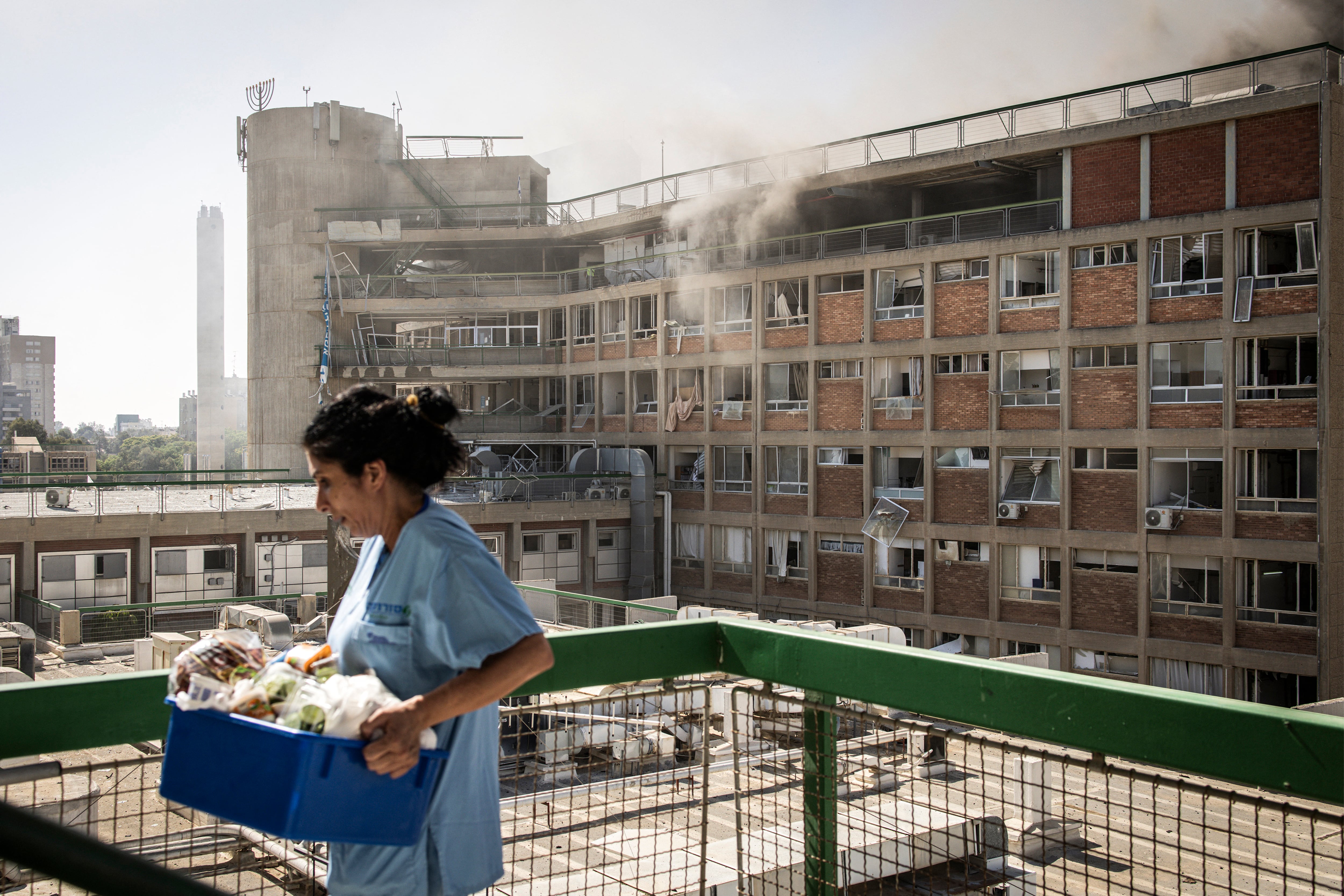 Una enfermera transporta suministros médicos frente a un edificio con columnas de humo en el Hospital Soroka tras un ataque con misiles de Irán en Beersheba, al sur de Israel, el 19 de junio de 2025. (Foto de JOHN WESSELS / AFP).
