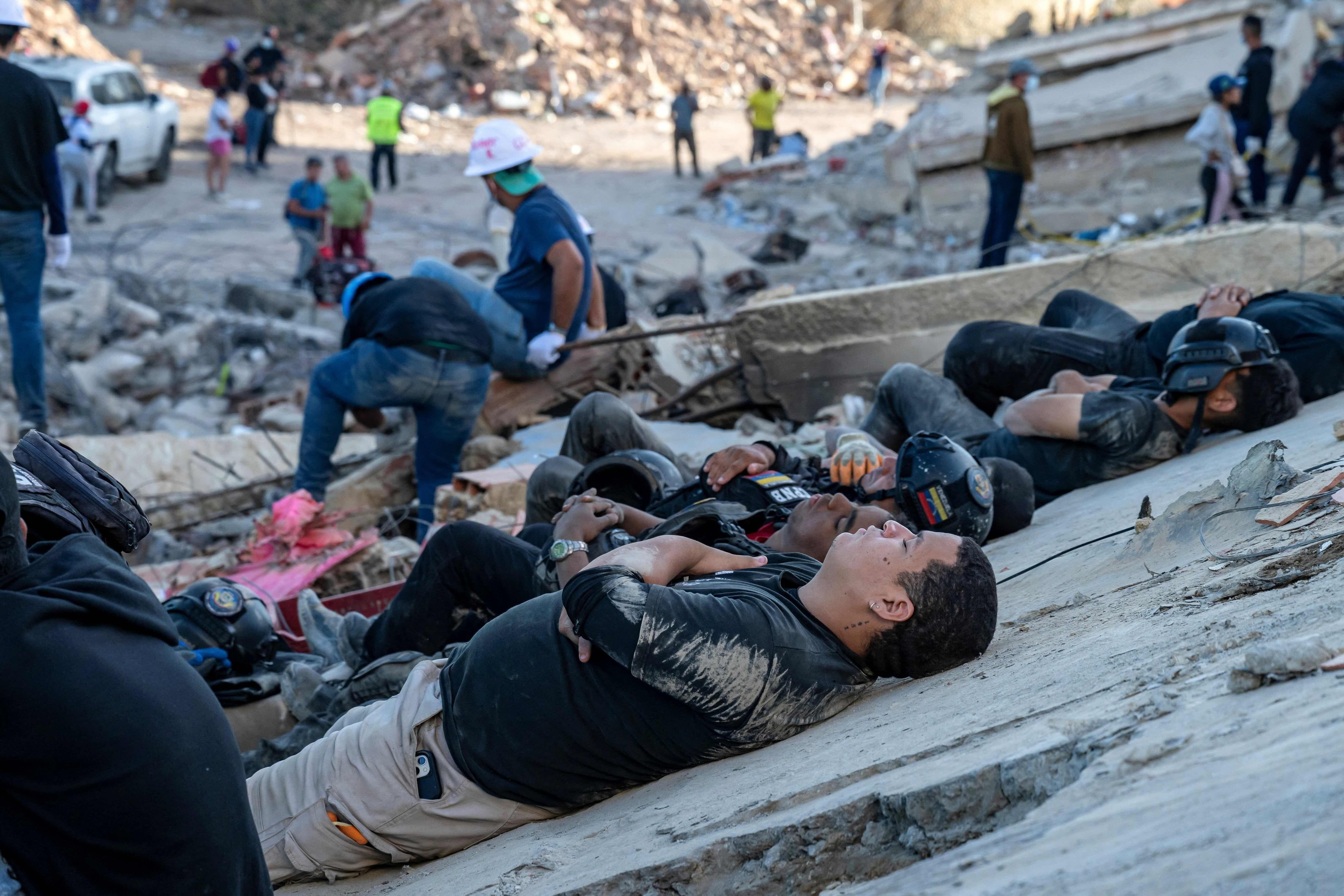 Rescatistas agotados descansan sobre una gran plancha de concreto que es parte de los escombros de un edificio colapsado.