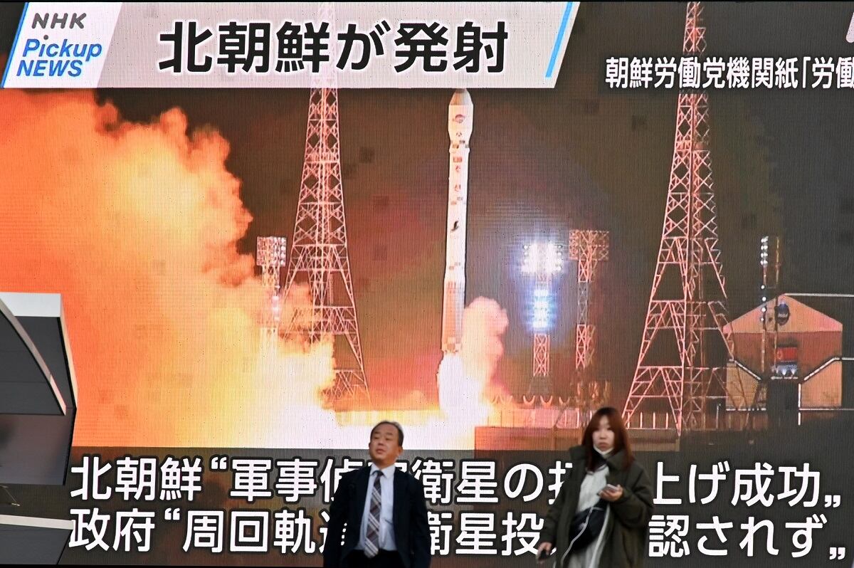 Peatones pasan junto a una pantalla que muestra el lanzamiento del satélite de reconocimiento de Corea del Norte 'Malligyong-1', en el distrito de Akihabara de Tokio el 22 de noviembre de 2023. (Foto de Kazuhiro NOGI / AFP)