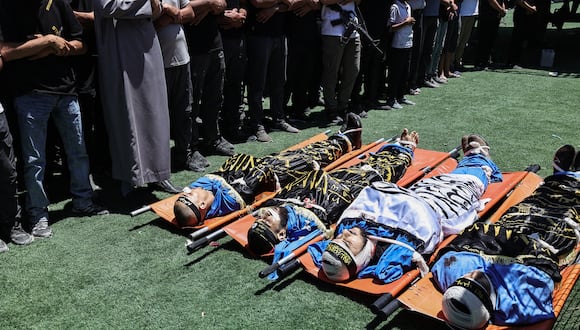 Los dolientes y los hombres armados rezan junto a los cuerpos de cuatro palestinos muertos un día antes en un ataque aéreo israelí contra el campo de refugiados de Nur Shams, cerca de Tulkarem, en la Cisjordania ocupada, durante su funeral en el campo el 3 de julio de 2024. (Foto de Zain JAAFAR / AFP)