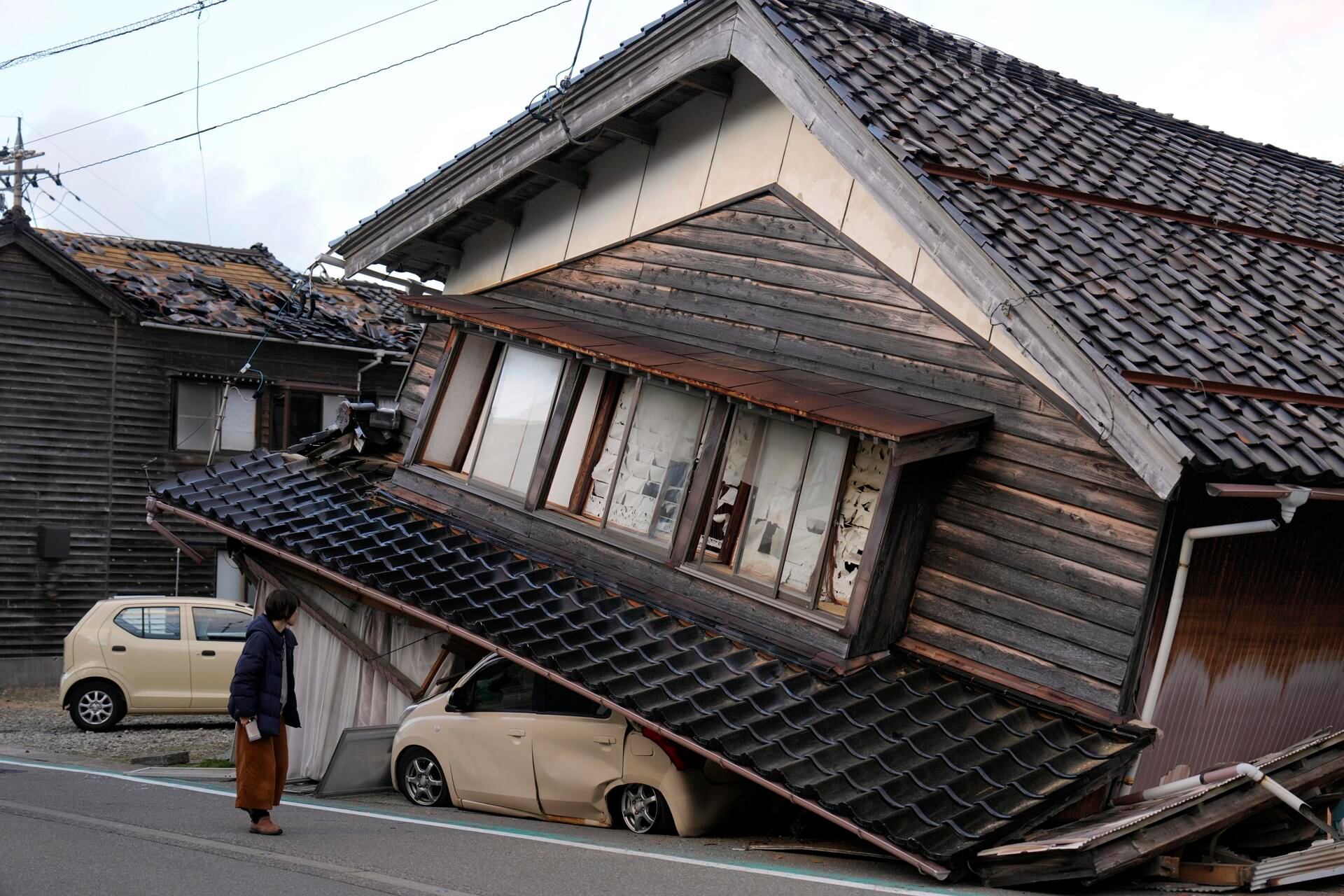 Una mujer observa una vivienda y vehículos dañados tras un fuerte terremoto en Tohi Town, en la península de Noto, Japón, este 2 de enero de 2024. (EFE/FRANCK ROBICHON).