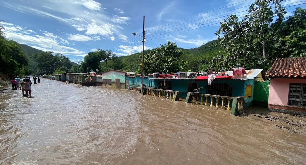 La gente se encuentra afuera de sus casas inundadas después de que un río creciera debido a las fuertes lluvias tras el paso del huracán Beryl en el estado Sucre, Venezuela. (Foto de Víctor GONZÁLEZ / AFP).