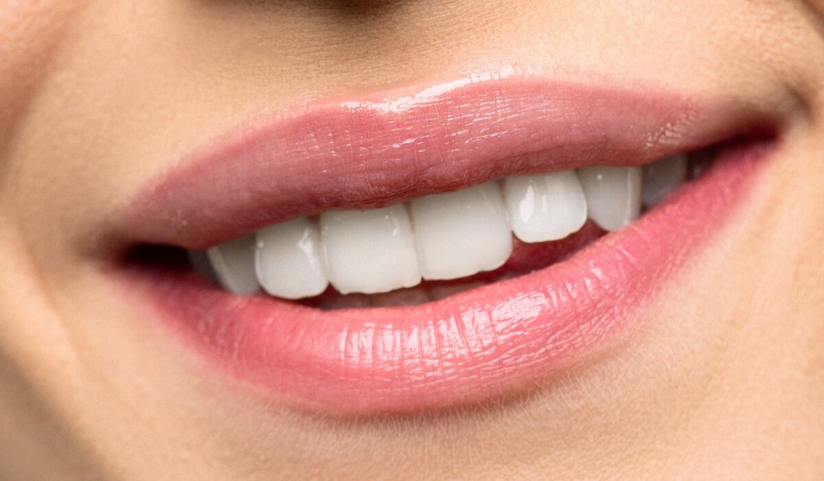 Primer plano de mujer con lápiz labial rosa sonriendo. (Imagen: Pexels)