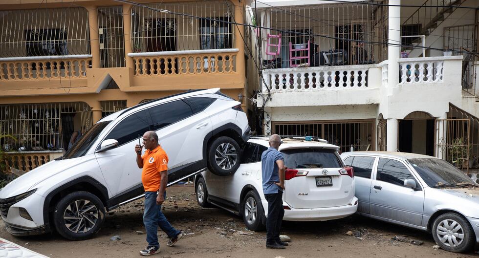 Personas caminan junto a varios vehículos que fueron arrastrados por la corriente en Santo Domingo, República Dominicana, afectada por lluvias torrenciales. (EFE/Orlando Barría).