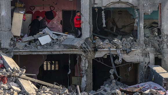 Los palestinos inspeccionan los daños entre los escombros de un edificio donde, según informes, dos rehenes fueron retenidos antes de ser rescatados durante una operación de las fuerzas de seguridad israelíes en Rafah, en el sur de la Franja de Gaza, el 12 de febrero de 2024, en medio de batallas en curso entre Israel y el grupo militante Hamás. (Foto de SAID KHATIB / AFP)