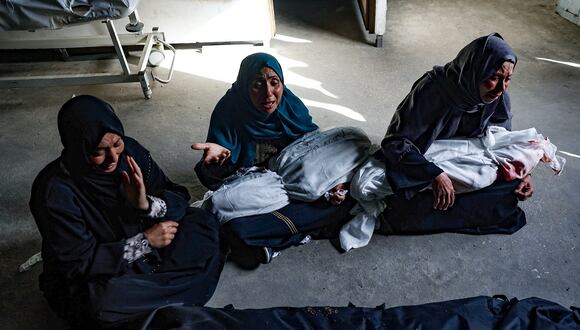 Mujeres palestinas sostienen los cuerpos amortajados de los niños muertos en los bombardeos israelíes, en una clínica de salud en el área de Tel al-Sultan en Rafah, en el sur de la Franja de Gaza, el 26 de mayo de 2024. (Foto de Eyad BABA / AFP)