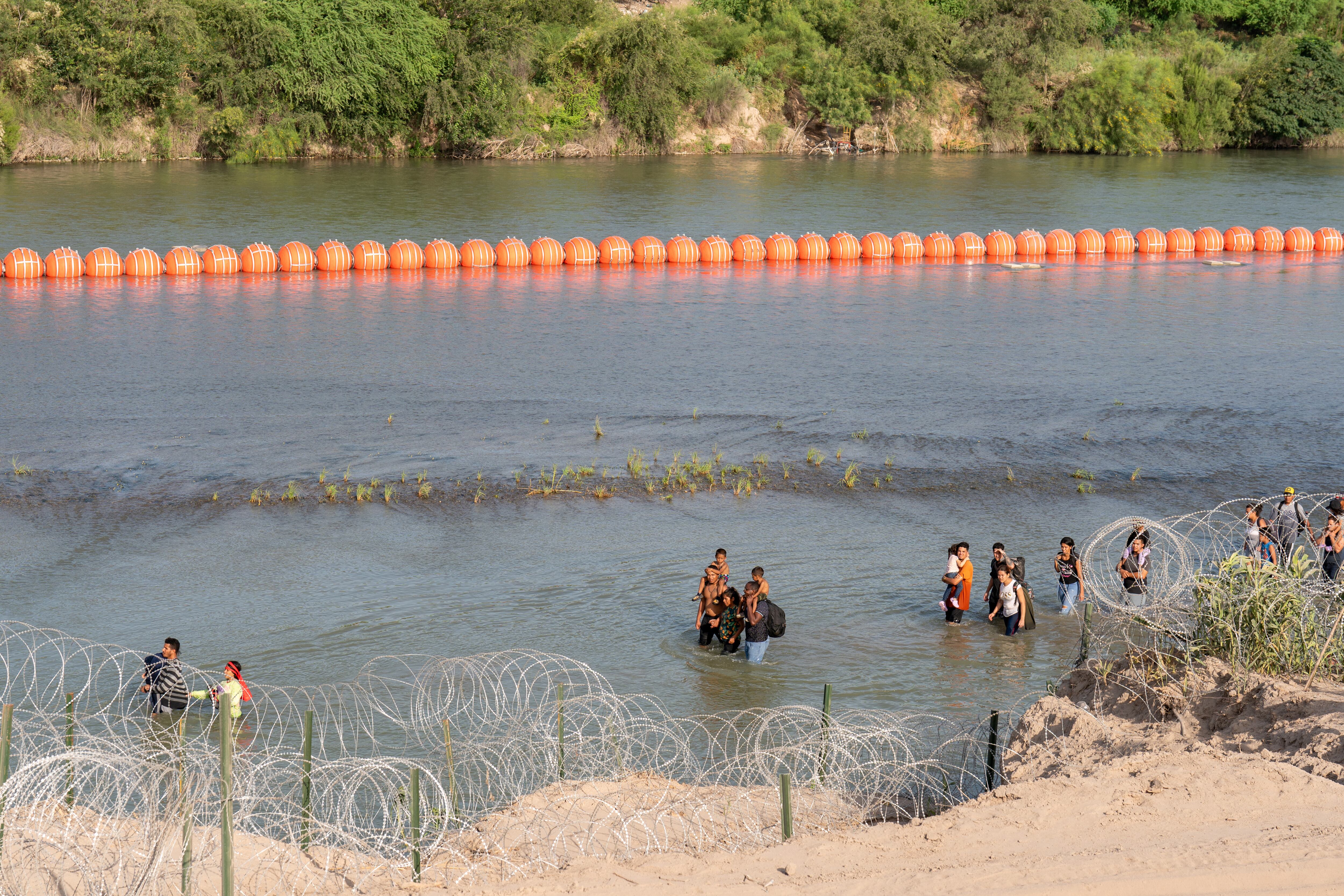 Migrantes caminan junto a una cadena de boyas colocadas en el agua a lo largo de la frontera del Río Grande con México en Eagle Pass, Texas. (Foto: AFP)