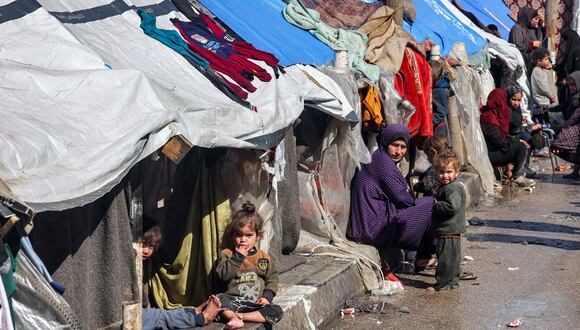 Una mujer y niños se sientan afuera de tiendas de campaña que albergan a palestinos desplazados en Rafah, en el sur de la Franja de Gaza, el 8 de febrero de 2024, en medio del conflicto en curso entre Israel y el grupo militante palestino Hamás. (Foto de Mohammed ABED / AFP)